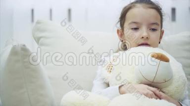 小迷人的女孩坐在沙发上，拥抱着她的大毛绒朋友，叹了口气。 她似乎很沮丧和担心。