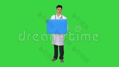 微笑男医生穿着听诊器拿着绿色屏幕上的空白海报，色度键。