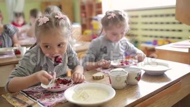 双胞胎女孩坐在幼儿园的桌子旁吃沙拉。 在学前班吃饭羡慕..