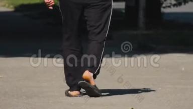 一个人光着<strong>脚</strong>穿着黑色运动裤和拖鞋走在街上。 夏日温<strong>暖</strong>的一天。 阳光。 休闲服。 无正面