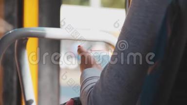 一个穿着浅色针织上衣的女孩手里拿着一部手机。 在乘客公共汽车停车时使用智能手机。 一个女人在看