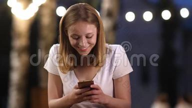年轻迷人的有兴趣的女孩正在夏天的晚上在智能手机上输入信息，微笑着交流