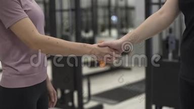 <strong>未被</strong>识别的女教练和客户在健身房的健身前握手。 积极运动的概念