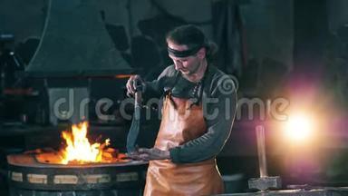 职业铁匠看着一把金属刀，站在一个<strong>锻造</strong>厂。