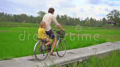 一个年轻人和他的小儿子骑着自行车穿过美丽的稻田。 前往东南亚构想