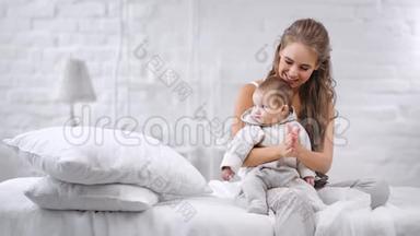 可爱的微笑的年轻妈妈玩着可爱的小宝宝拍手，温柔