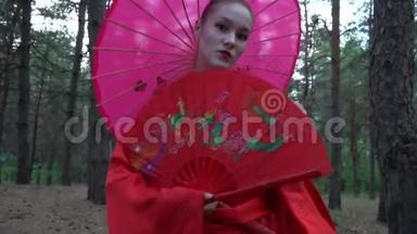 一个穿着红色和服的美丽的艺妓看着相机，慢悠悠地走在针叶林中