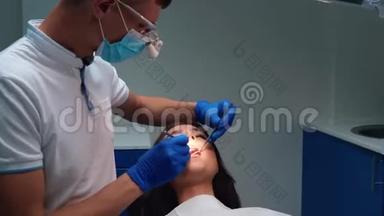 戴着医用蓝色手套、口罩和眼镜的年轻牙医用牙镜和牙坝`病人的牙齿