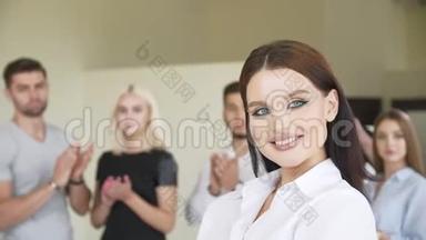 一个穿着白衬衫的动作缓慢的年轻美女在一群年轻人的背景下摆姿势微笑