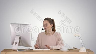 漂亮的年轻休闲女士戴着耳机，在渐变背景下在电脑上工作。