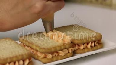 一个女人正在用饼干和奶油准备糕点。 将奶油应用于糕点袋中的饼干。 特写镜头