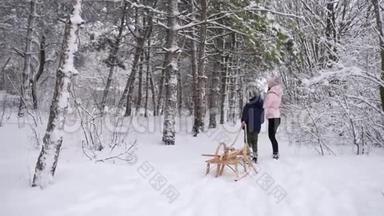 穿着温<strong>暖</strong>衣服的可爱男孩和他的母亲在下雪的<strong>冬日</strong>拉着木制的老式雪橇散步。 一个小男孩滑了进去