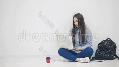 可爱的年轻亚洲女士坐在地板上，以洛托斯的姿势，在互联网上搜索，挥手<strong>问好</strong>。 学校用品