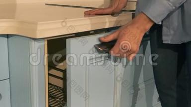 女人`手在现代陈列室的厨房里打开一扇家具冰柜门。 关闭家具店的女人