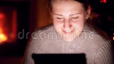 4k特写视频：微笑的年轻女子坐在黑暗的客厅里，看着数码平板电脑屏幕