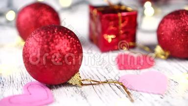 白色木桌上的圣诞树装饰品。 红色的球和礼品盒，粉红色的心。 圣诞树亮灯亮灯