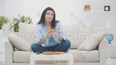 饥饿的女人正在打开电视节目，而坐在沙发上。 她在吃披萨。 4K.