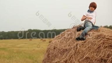 一个十几岁的男孩坐在草地上的干草堆上。 小帅哥在干草堆上休息
