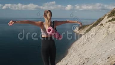 从侧面看，身穿运动服的女人站在悬崖边上，张开双臂