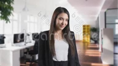 微笑的年轻女子正在看镜头。 她站在后台的现代办公室里。