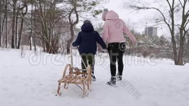 穿着温暖衣服的可爱男孩和他的母亲在下雪的冬日拉着木制的老式雪橇散步。 一个小男孩滑了进去