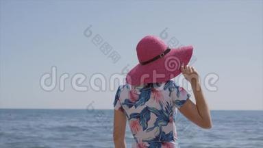 孤独优雅的女人，穿着蓝色的泳衣，粉红色的帽子，站在海边，看着地平线