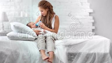 赤脚<strong>微笑</strong>的女人在白色房间里<strong>躺</strong>在床上，享受着从奶瓶中喂养新生<strong>婴儿</strong>的乐趣