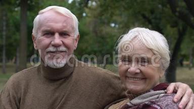 微笑成熟的夫妇坐在公园的长凳上拥抱，社保