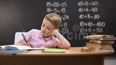 坐在书桌前的无聊的学生，不愿意准备数学作业