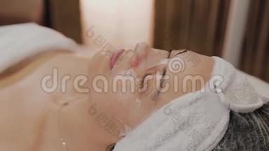 女人躺在沙发上，在美容院戴着透明的织物抗衰老面具。
