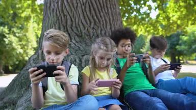 孩子们玩小玩意，<strong>坐在</strong>公园的<strong>树下</strong>，男孩在相机里微笑，应用程序