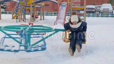 冬季活动时，玩耍的女孩在雪地操场上打开旋转木马秋千。 女孩骑着旋转木马围着孩子