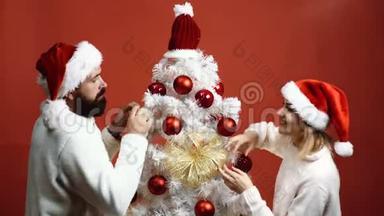 年轻夫妇戴着`顶帽子，用<strong>红色背景装饰圣诞</strong>树. 背景。 恋爱中的情侣。 新年