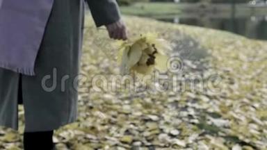 女人走在秋天的公园里，手里拿着一束黄叶。 落叶开始了