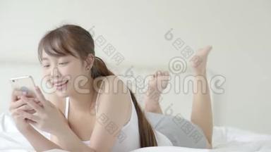 美丽的肖像年轻的亚洲女人微笑着躺着看智能手机阅读社交网络与享受床上卧室