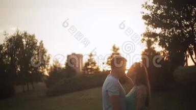 爱的一对情侣在夕阳下在阳光下接吻。 两个情人在公园日落时接吻的剪影。