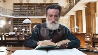 坐在图书馆桌子旁翻书页的一个专注的大胡子老头
