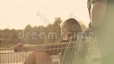 后景。 快乐的年轻情侣恋爱中的男人和女人在超市停车场的推车里嬉笑打闹