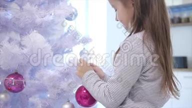 歪歪扭扭的视频，美丽的小女孩在前面的圣诞树，并把一个玻璃泡在其中一个