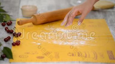 女人`手把面团擀在厨房的桌子上，用樱桃做馅饼。