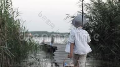 快乐的童年，带着钓竿和篮子吃零食的漂亮小男孩沿着桥走到<strong>芦苇丛</strong>中的码头，去钓鱼
