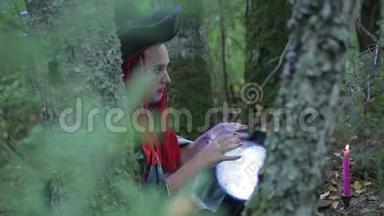 一个红头发的女巫和森林里的帽子用发光的球和燃烧的蜡烛做魔法。