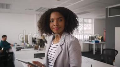 快乐年轻的职业女商人在办公室里使用数字平板电脑的肖像和在后台工作的同事