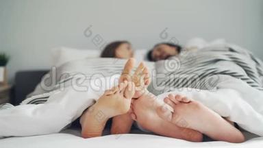 当人们躺在一起的时候，女孩和男人的双脚在床上用毯子抚摸