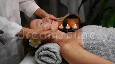美容师用玉石做专业的面部按摩。 在水疗中心接受面部按摩的妇女