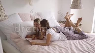 两个穿着同样睡衣的年轻女人躺在床上看着平板电脑上的<strong>照片</strong>。 在家里休闲。 母鸡<strong>党</strong>