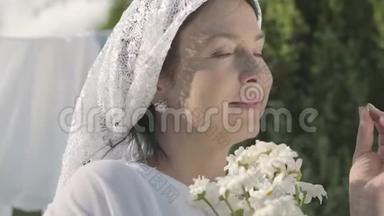可爱的成熟女人，头上戴着白色披肩，在户外的晾衣绳上撕下雏<strong>菊花瓣</strong>。 华盛顿。 积极正面