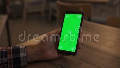一名男子手持绿色模拟屏幕智能手机的特写镜头。使用应用程序。现代手机。在背景中舒适