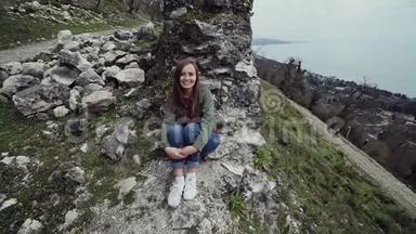 可爱的女孩坐在海边的一座山上的一座古老堡垒的墙边