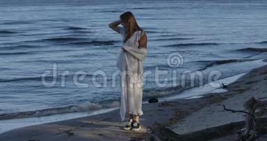 年轻的高加索女人站在海滩上看着海浪。 体贴的女孩在户外度过夏天的夜晚。